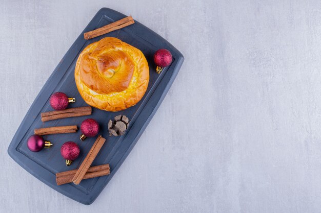 Delicioso bollo, cono de ciprés, canela y adornos navideños sobre fondo blanco.