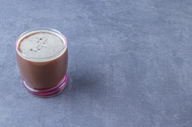 Delicioso café en un vaso, sobre fondo azul.