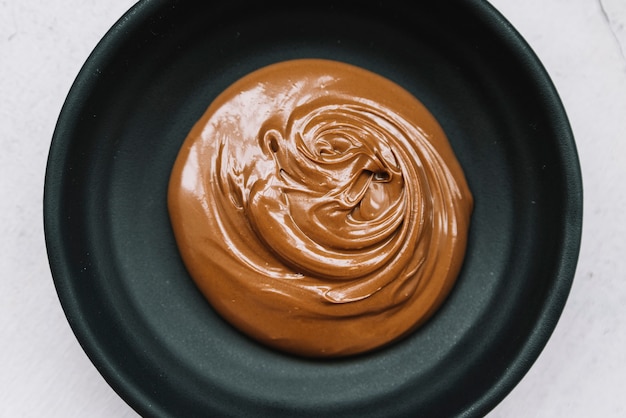 Delicioso chocolate derretido en un tazón negro sobre fondo blanco