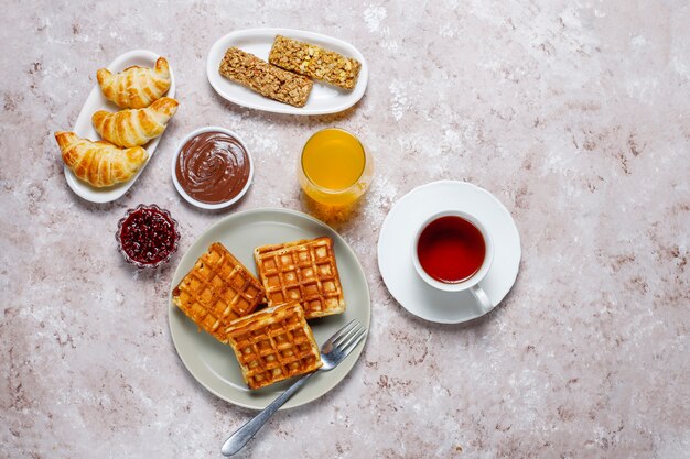 Delicioso desayuno con café, jugo de naranja, gofres, cruasanes, mermelada, pasta de nueces a la luz, vista superior