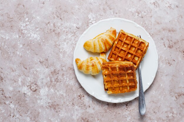 Delicioso desayuno con café, jugo de naranja, gofres, cruasanes, mermelada, pasta de nueces a la luz, vista superior