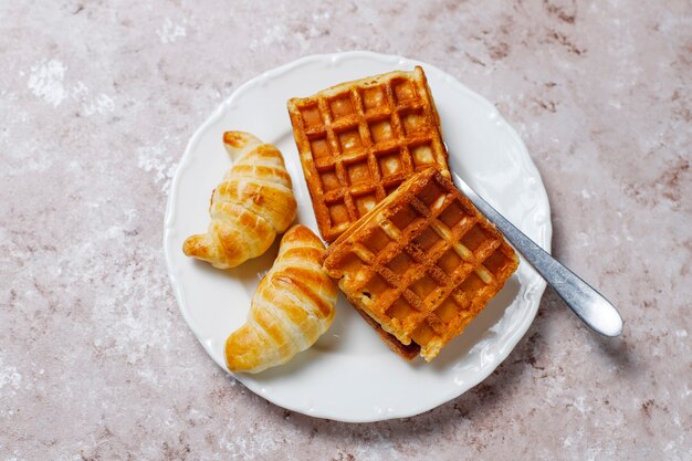 Delicioso desayuno con café, jugo de naranja, gofres, cruasanes, mermelada, pasta de nueces a la luz, vista superior