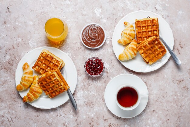 Delicioso desayuno con café, jugo de naranja, gofres, cruasanes, mermelada, pasta de nueces a la luz, vista superior