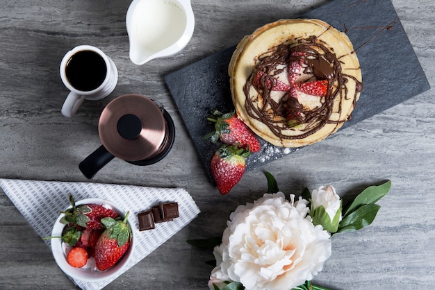 Delicioso desayuno con café, panqueques con fresas y chocolate en la mesa