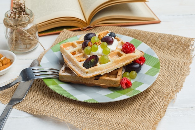 Delicioso desayuno con gofres y frutas cerca de un libro.