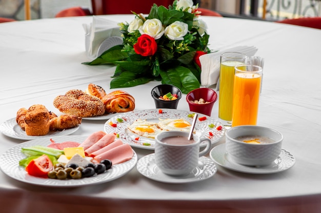 Delicioso desayuno en una mesa con ensalada, huevos fritos y pastelería vista lateral sobre un fondo blanco.