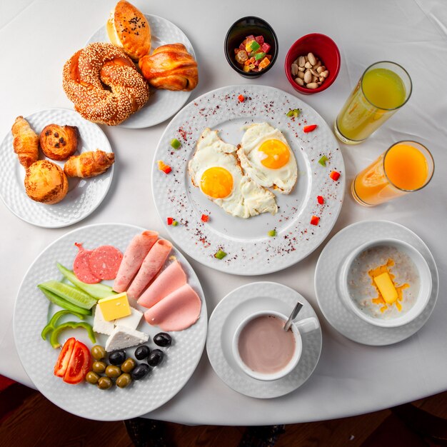 Delicioso desayuno en una mesa con ensalada, huevos fritos y pastelería vista superior sobre un fondo blanco.