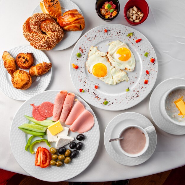 Delicioso desayuno en una mesa con ensalada, huevos fritos y pastelería vista superior sobre un fondo blanco.