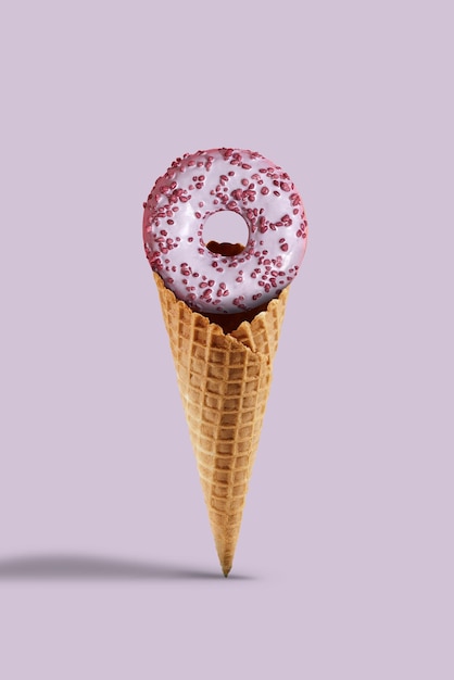 Delicioso donut espolvoreado y glaseado en cono de oblea dulce sobre fondo lila. Concepto de comida, golosinas y nutrición poco saludable. Cerrar, copiar espacio