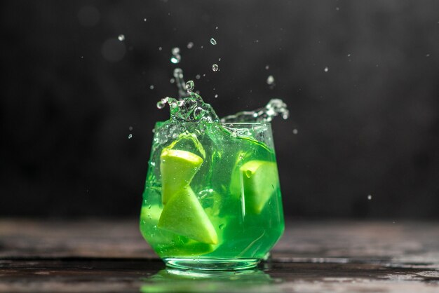 Delicioso jugo en un vaso con limones de manzana sobre fondo oscuro