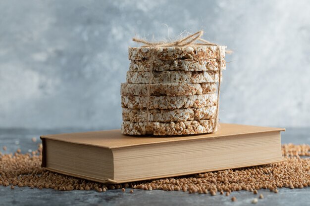 Delicioso pan crujiente, trigo sarraceno crudo y libro sobre superficie de mármol