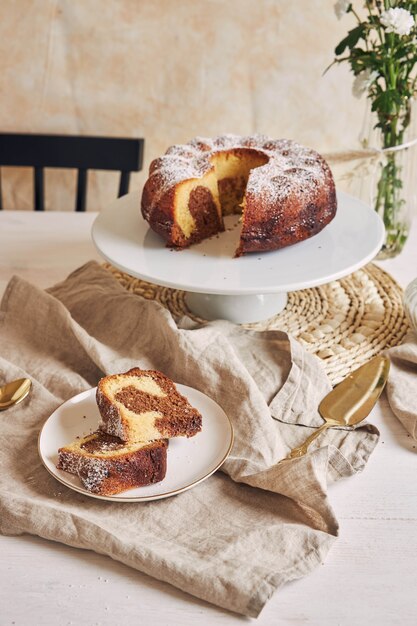 Delicioso pastel de anillo puesto en un plato blanco y una flor blanca cerca