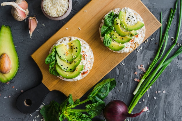 Delicioso pastel de arroz con queso crema y aguacate sobre tabla de madera con vegetales orgánicos