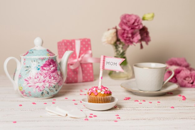 Delicioso pastel con bandera decorativa con título de mamá cerca de tetera, flores y taza