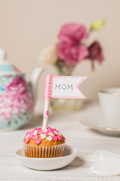 Delicioso pastel con bandera decorativa con título de mamá cerca de tetera y flores