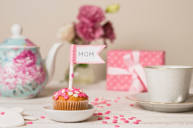 Delicioso pastel con bandera decorativa con título de mamá cerca de tetera y taza