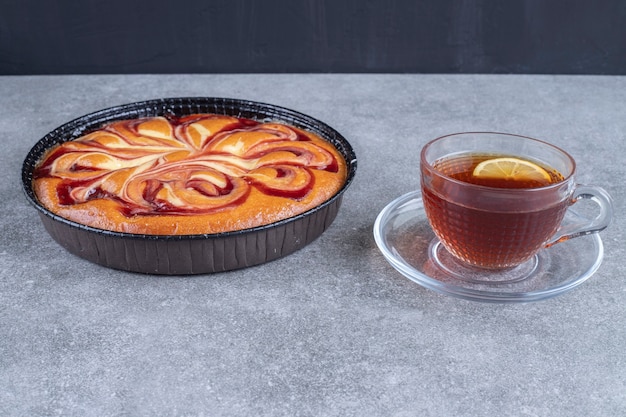 Delicioso pastel con bayas y taza de té en la superficie de mármol