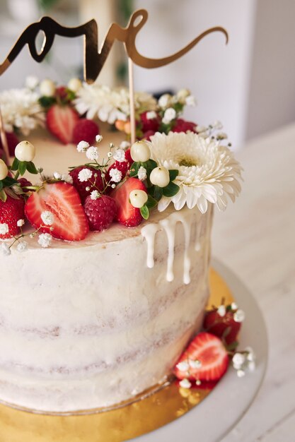 Delicioso pastel de bodas blanco con frutos rojos, flores y adorno de torta