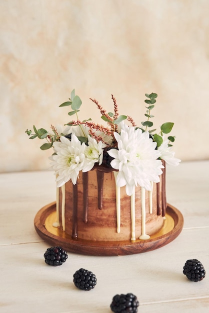 Delicioso pastel de chocolate blanco y marrón con flores y moras en una mesa