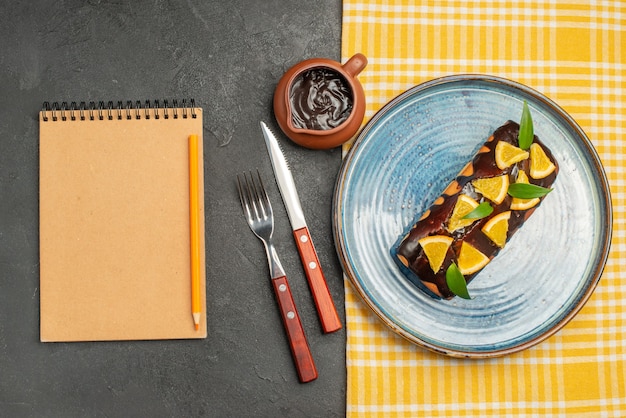 Delicioso pastel decorado con naranja y chocolate servido con tenedor y cuchillo y cuaderno