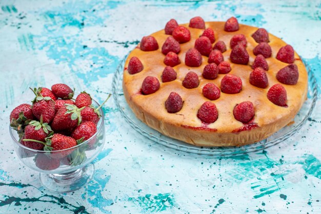 delicioso pastel de fresa en forma redonda con frutas y junto con fresas rojas frescas en un escritorio azul brillante, masa de pastel, bizcocho de fruta dulce