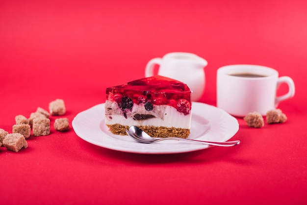 Delicioso pastel de gelatina y queso de fresa en un plato blanco con cubos de azúcar morena sobre fondo rojo