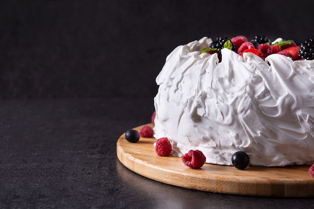 Delicioso pastel de Pavlova con merengue y bayas frescas sobre fondo negro