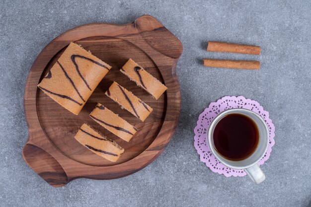 Delicioso pastel de rollo en placa de madera con taza de té