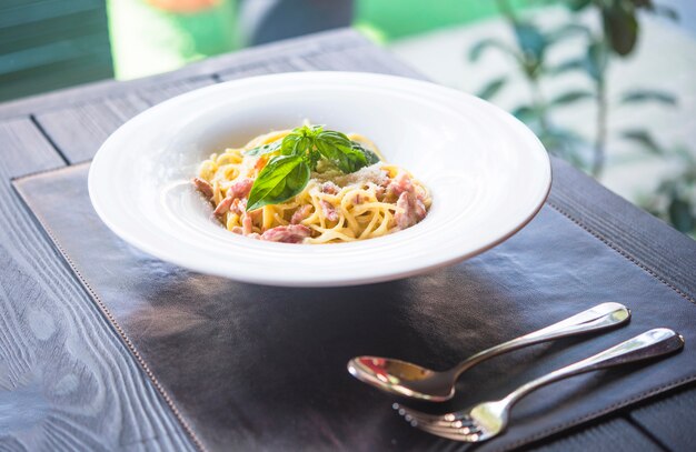Delicioso plato de espaguetis con carne y hojas de albahaca en mesa de madera
