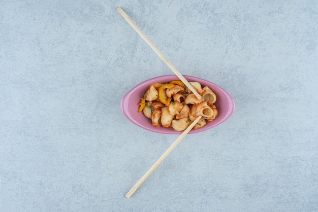 Delicioso plato rosa con macarrones y palillos sobre fondo oscuro. Foto de alta calidad