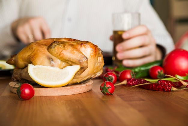 Delicioso pollo asado entero frente a un hombre sosteniendo un vaso de cerveza