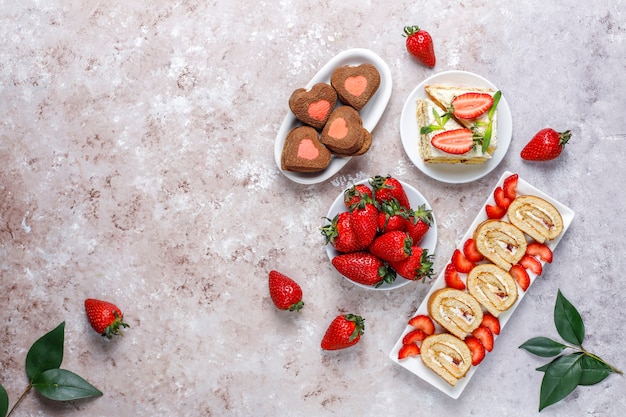 Delicioso rollo de pastel de fresa, galletas en forma de corazón, rebanadas de pastel con fresas frescas, vista superior