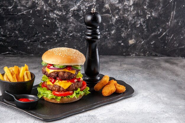 Delicioso sándwich casero y papas fritas con salsa de tomate nuggets de pollo en una pizarra en el lado derecho sobre una superficie gris angustiada