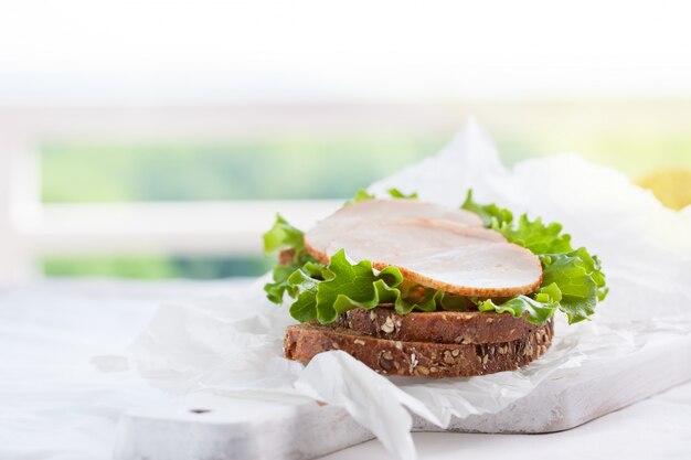 Delicioso sándwich hecho en casa con hojas de ensalada y jamón en una tabla de cortar