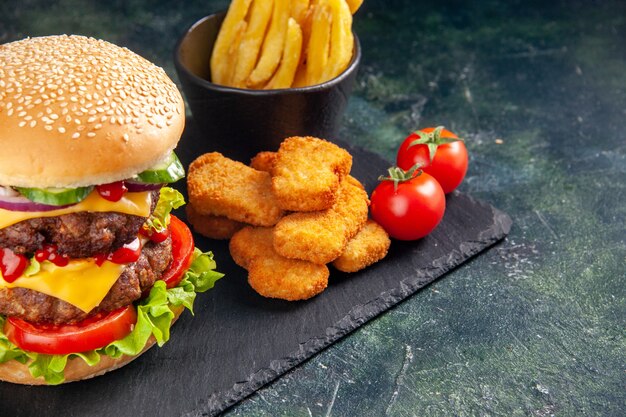 Delicioso sándwich y nuggets de pollo fritas en bandeja de color oscuro en el lado derecho sobre superficie negra