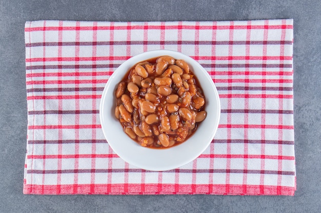 Foto gratuita delicioso tazón de frijoles horneados sobre un paño de cocina, sobre la superficie azul.