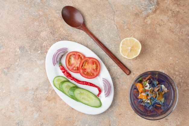 Delicioso té con pepino, tomate, rodaja de limón y cuchara en plato blanco