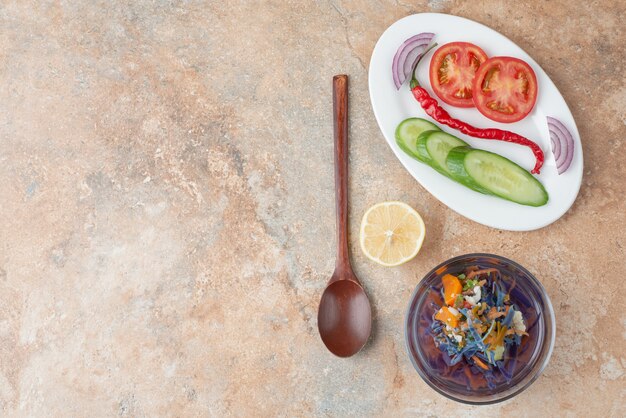 Delicioso té con pepino, tomate, rodaja de limón y cuchara en plato blanco