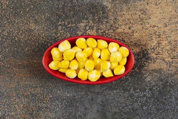 Deliciosos caramelos amarillos en tazón de fuente rojo.