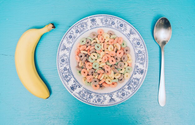 Foto gratuita deliciosos cereales en un plato con plátano y cuchara contra el fondo azul con textura