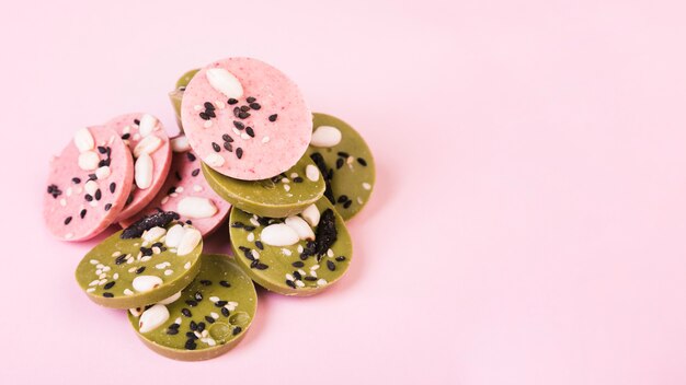 Deliciosos círculos de chocolate verde y rosa decorados con semillas sobre papel tapiz rosa