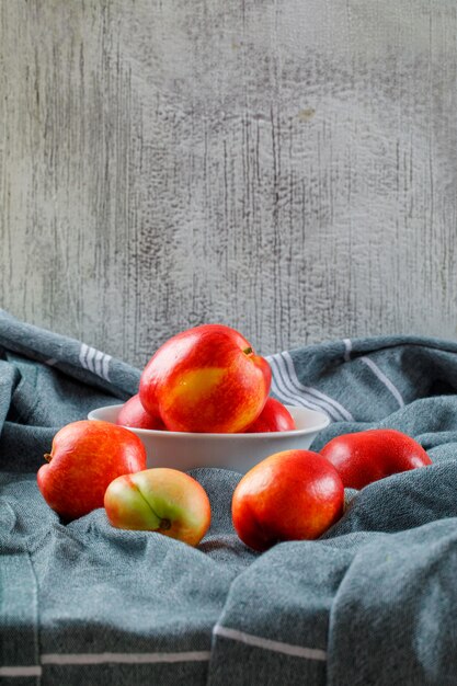 Deliciosos duraznos en un tazón blanco vista lateral sobre una textura de ropa y pared sucia