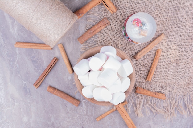 Deliciosos malvaviscos en una taza de madera con ramas de canela alrededor