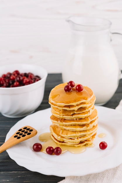 Deliciosos panqueques con miel y bayas de grosella roja en plato blanco