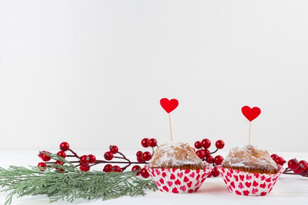 Deliciosos pasteles con corazones en varitas cerca de ramitas