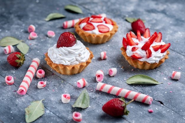 Deliciosos pasteles cremosos con fresas frescas y en rodajas junto con caramelos en gris, pastel de frutas dulce baya horneada