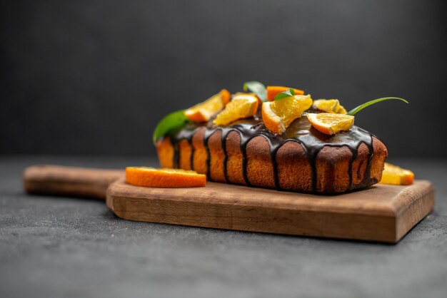 Deliciosos pasteles decorados con naranja y chocolate en la tabla de cortar de madera en el cuadro negro