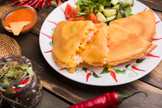 Deliciosos pasteles junto a la ensalada de verduras en un plato entre nachos con salsa y chili