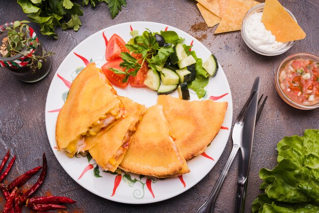 Deliciosos pasteles junto a la ensalada de verduras en un plato entre nachos con salsa y cubiertos