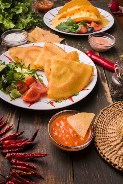 Deliciosos pasteles junto a ensaladas de verduras en platos entre nachos con salsas